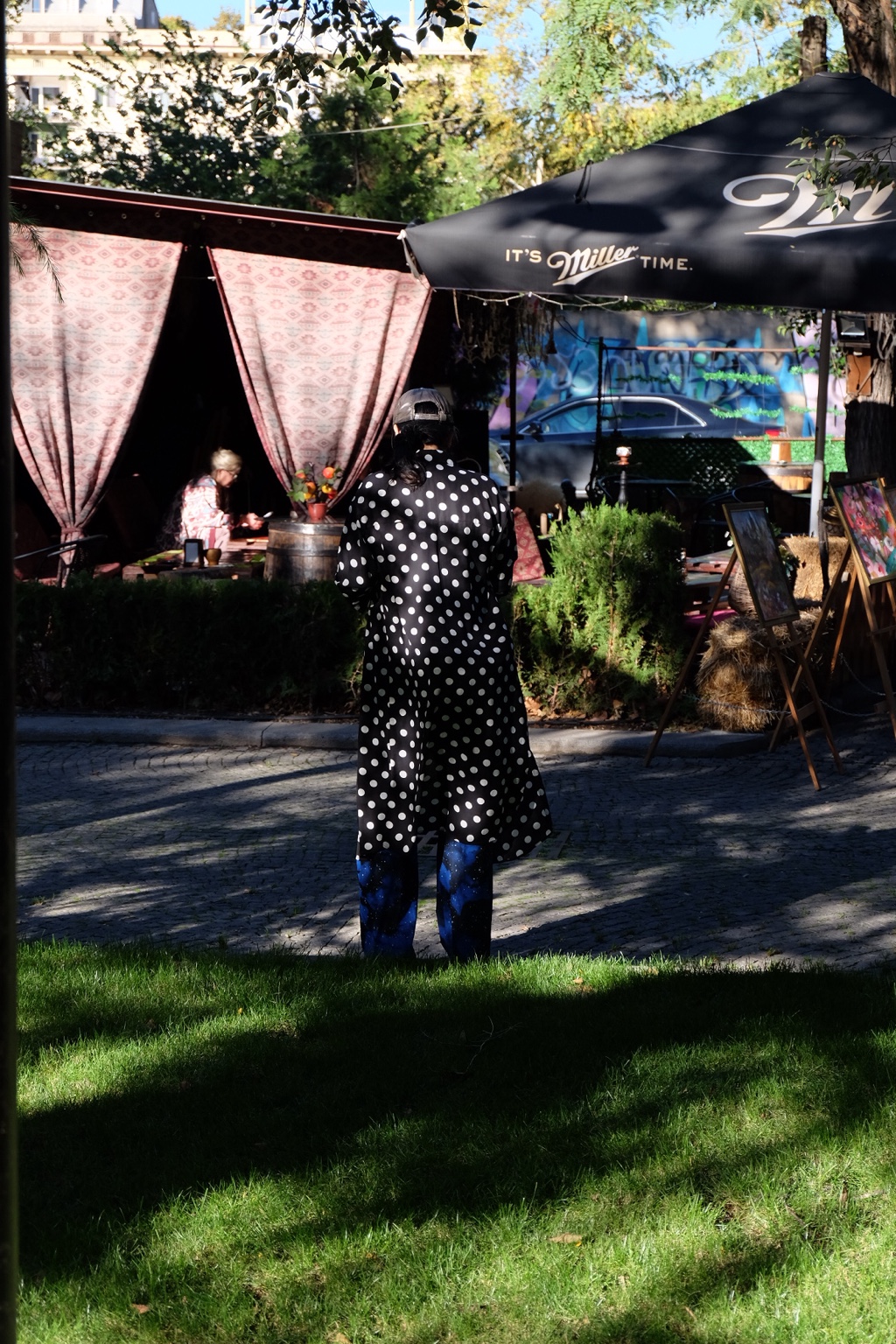 Person in a polka dot coat standing near an outdoor cafe