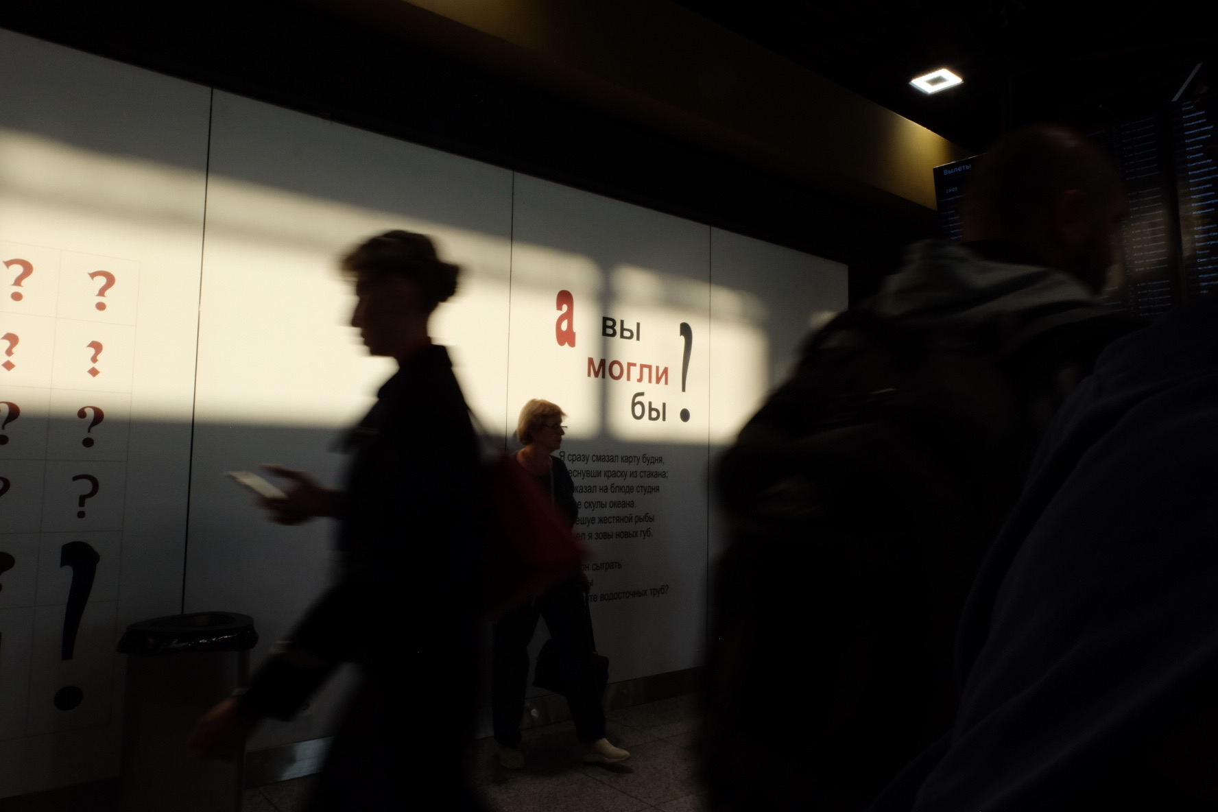 Blurred figures passing a lit question mark wall in the metro