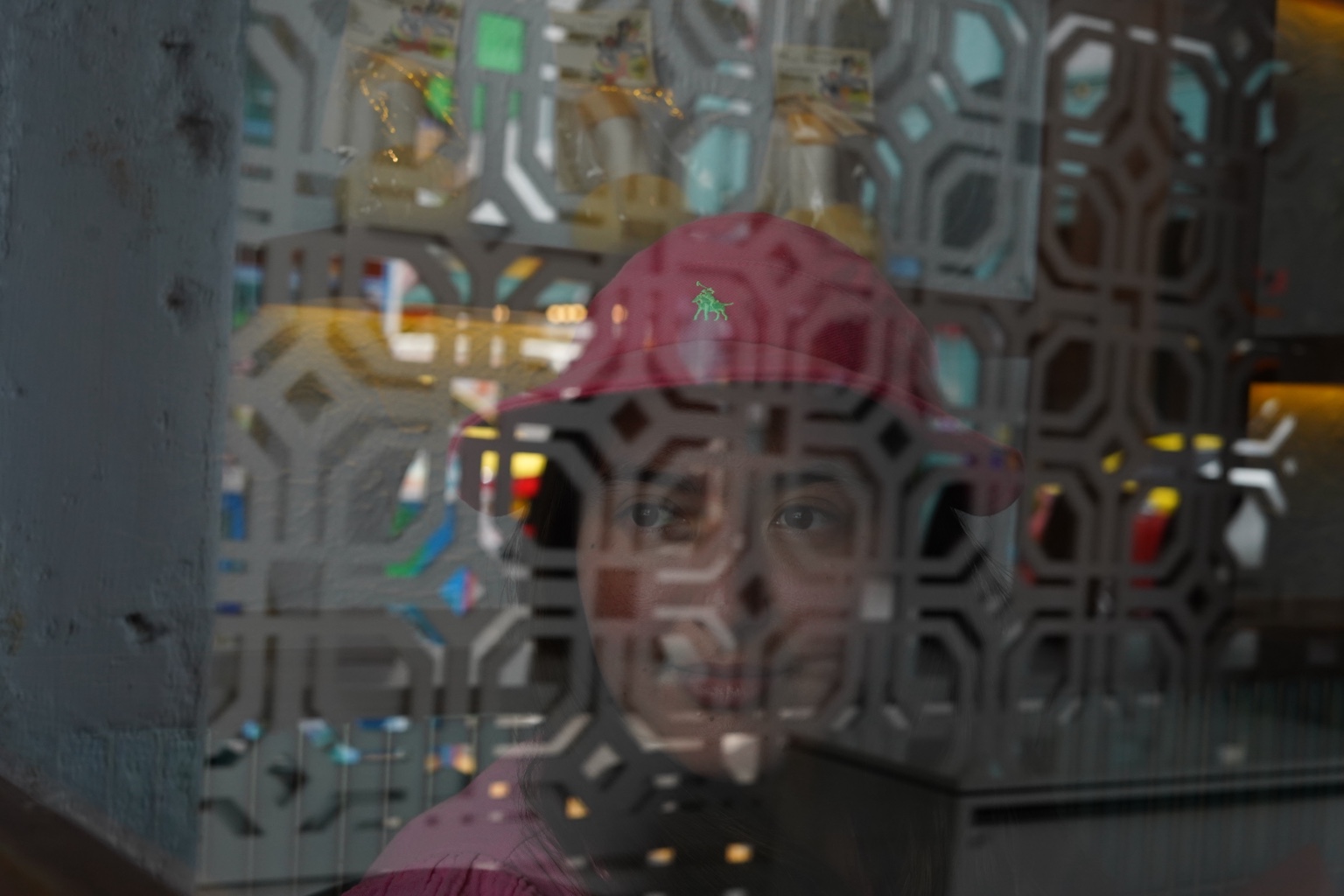 A face in a red hat seen through patterned glass reflections