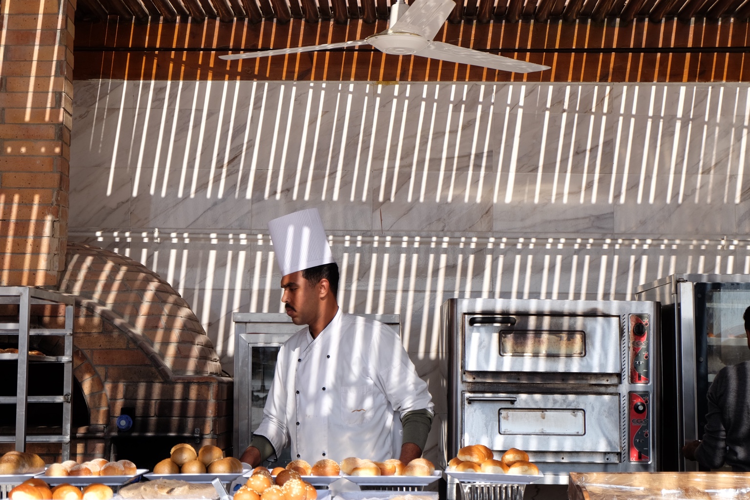 Chef working under striped shadows at a bakery counter