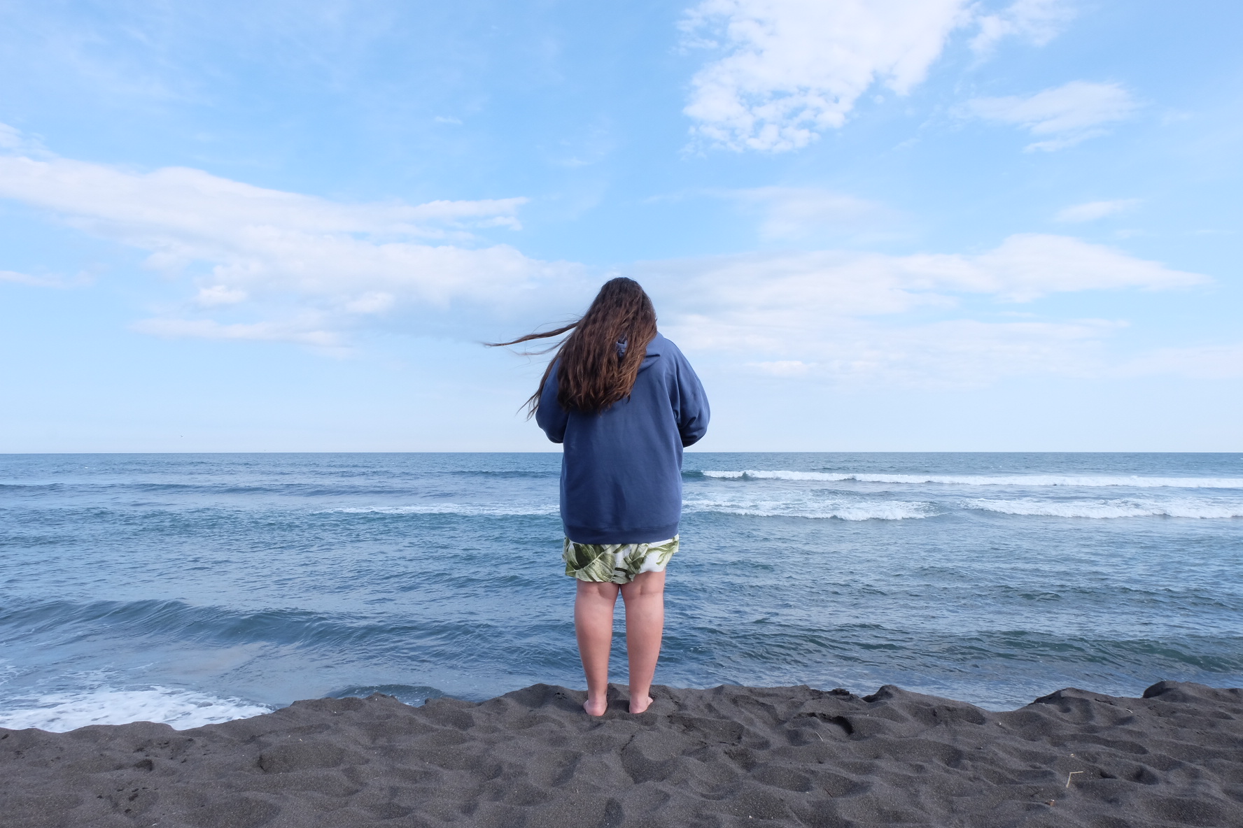 Person standing with their back to the camera facing the sea
