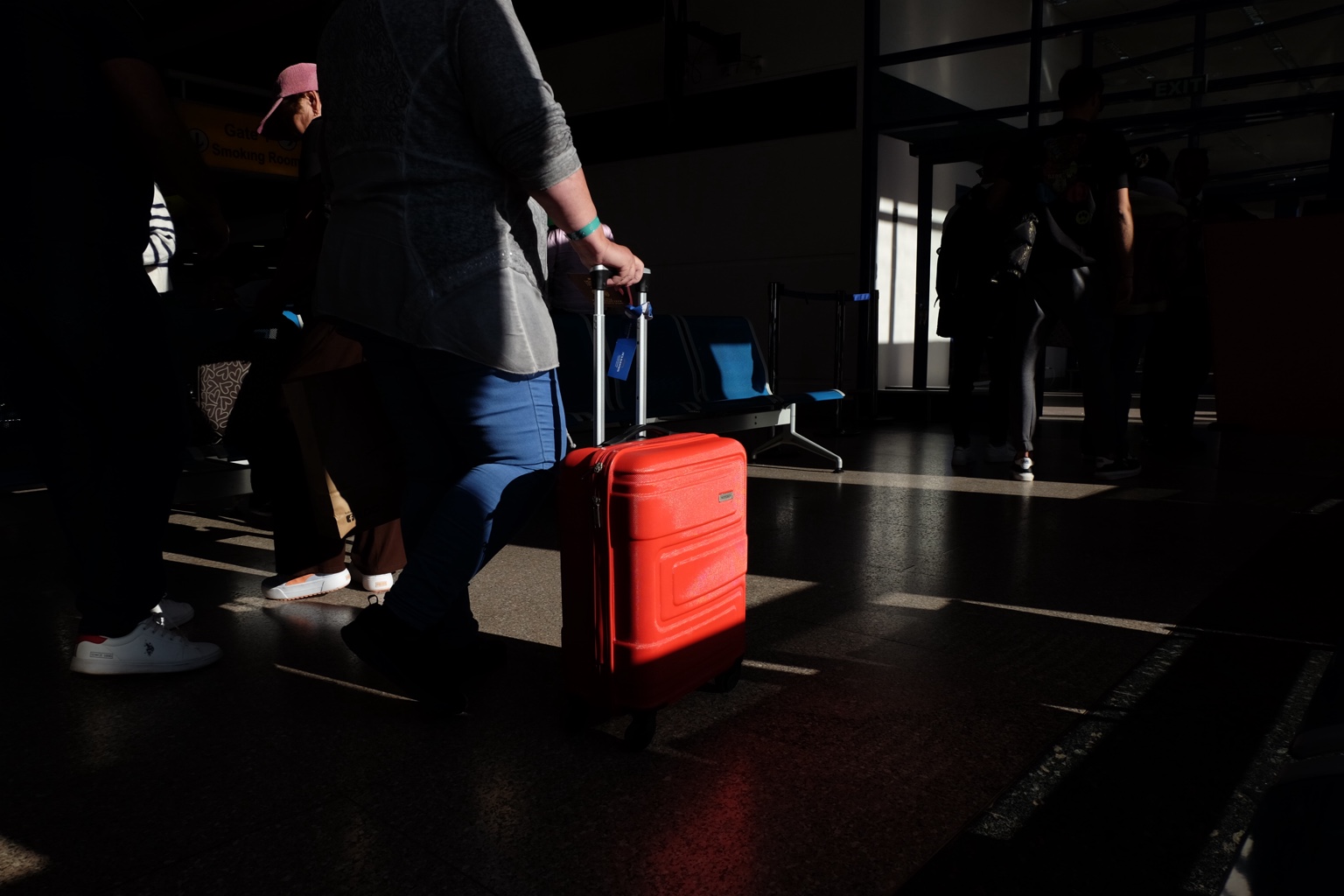 A red suitcase catching sunlight in a dark airport space