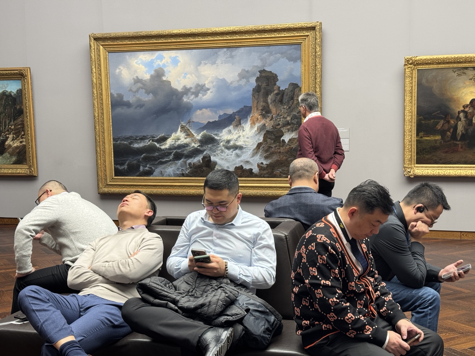 People resting with phones in front of framed paintings in a museum