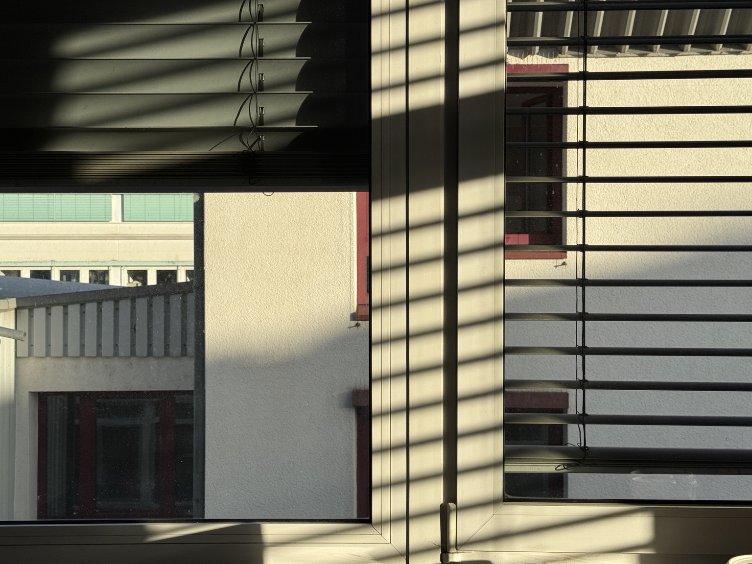 Window blinds casting graphic shadows across a building view