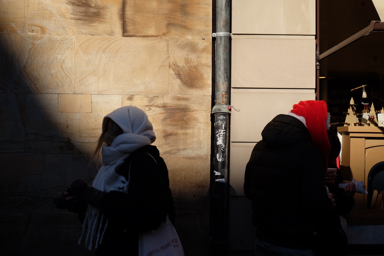 Two people in winter hats standing between shadow and shop light