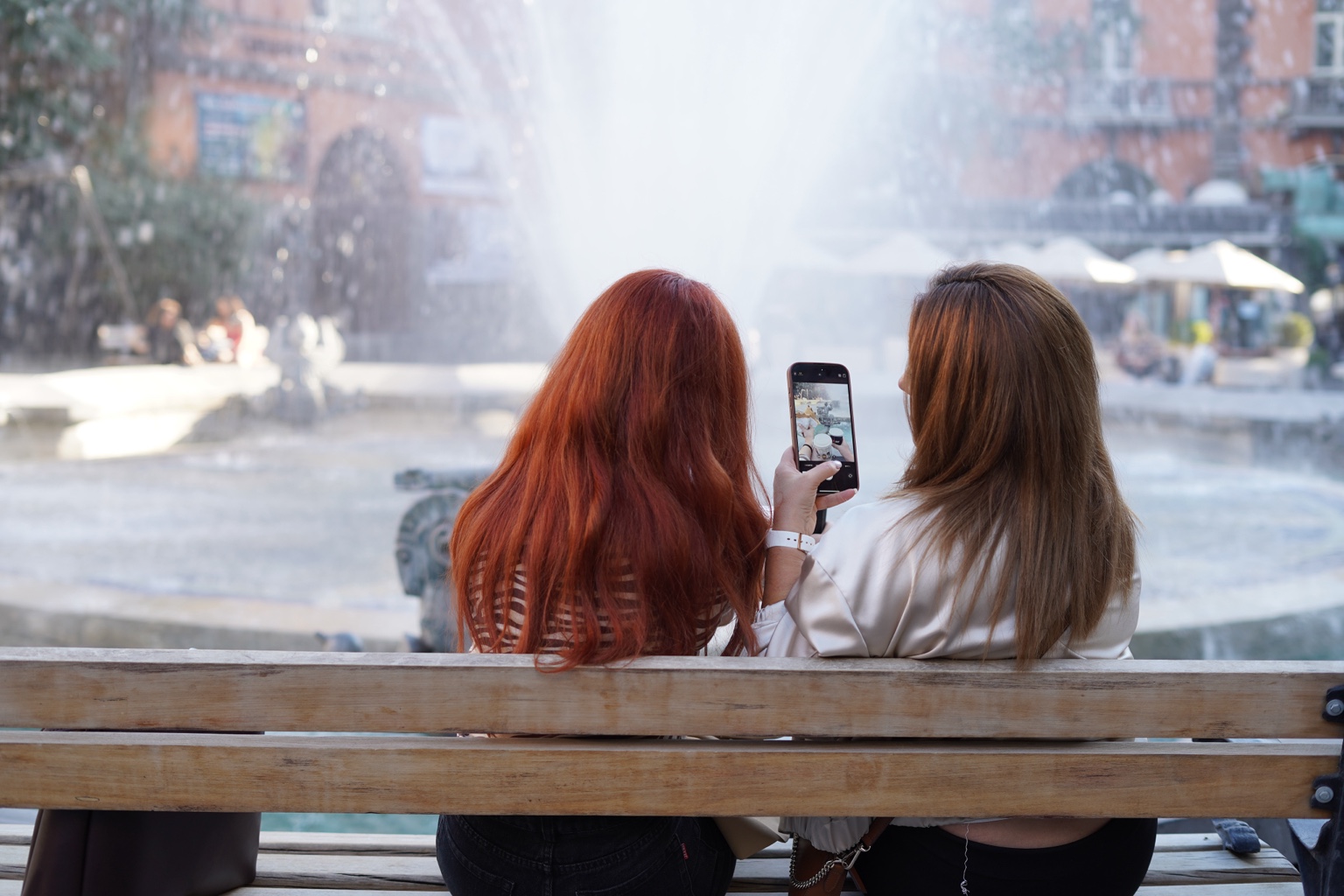 Two people on a bench looking at a phone near a bright fountain