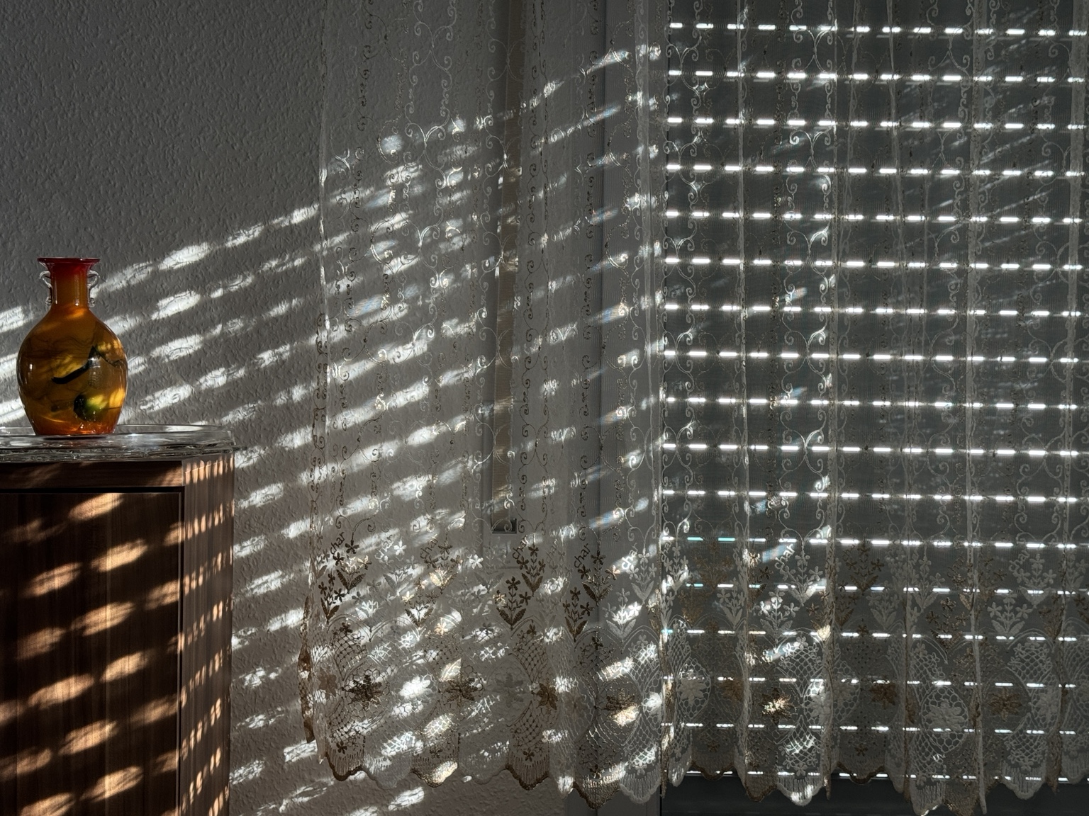 Amber vase and lace curtains covered in patterned window light