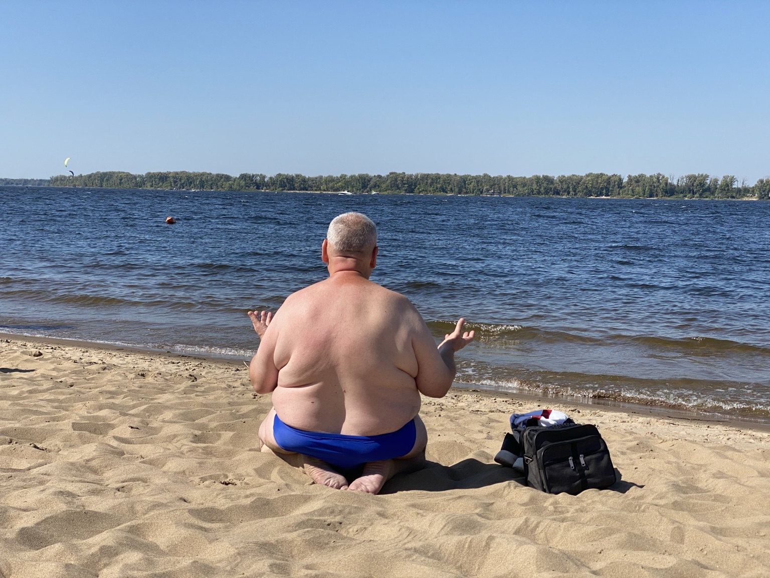 Man sitting on a beach with his back to the camera facing the water
